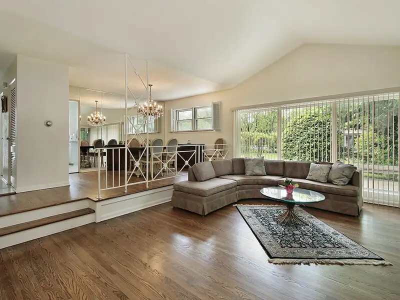 Classic sunken living room with a cozy sectional sofa, hardwood flooring, and an adjacent elevated dining area featuring chandeliers.