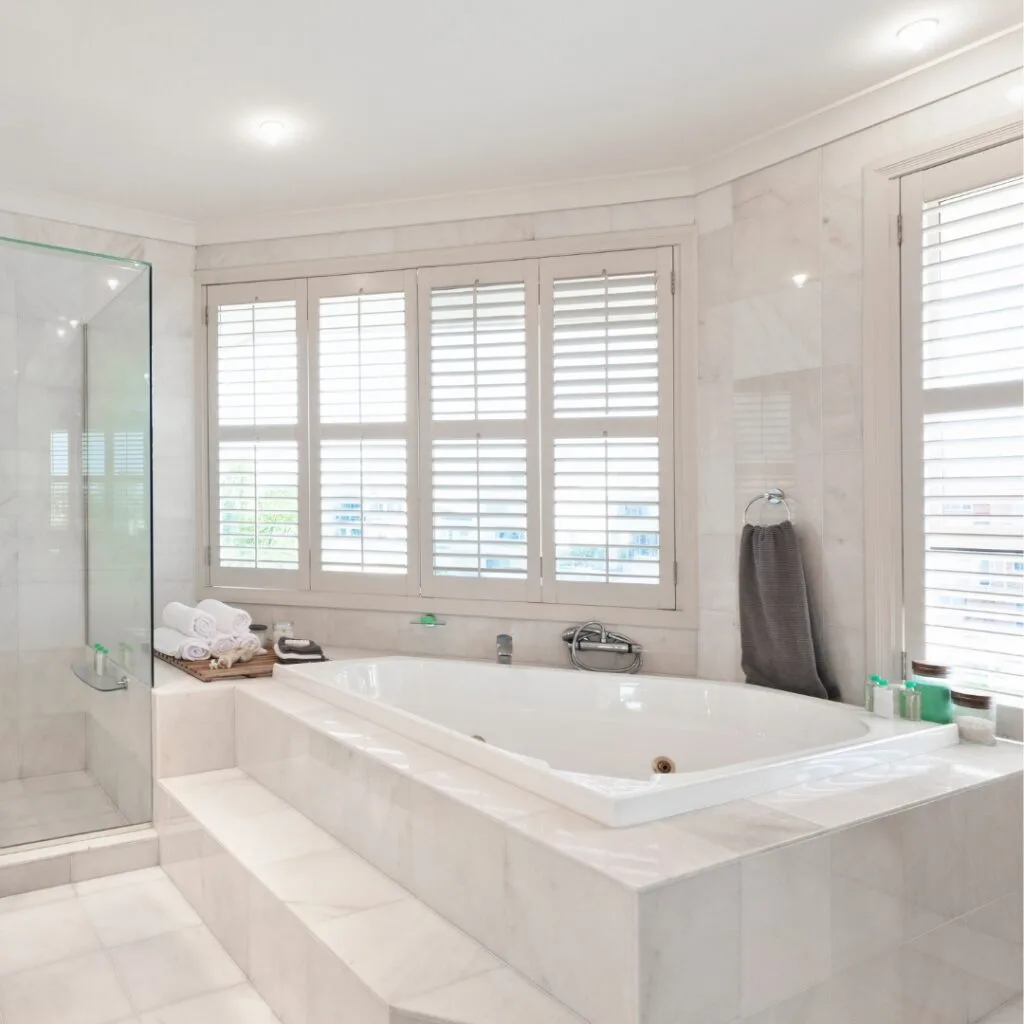 A white Jacuzzi bath remodel in a modern, spacious bathroom with marble-like tiles and a nearby glass shower.