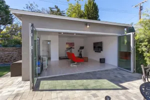 Stylish modern garage conversion featuring an open layout with glass doors, gym equipment, and a cozy entertainment area.